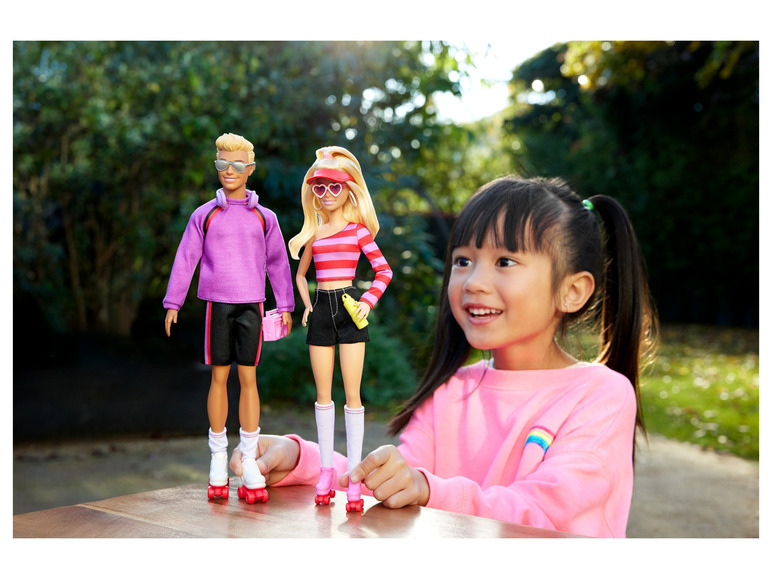Barbie und Ken Puppen mit Rollschuhen, gehalten von einem Kind.