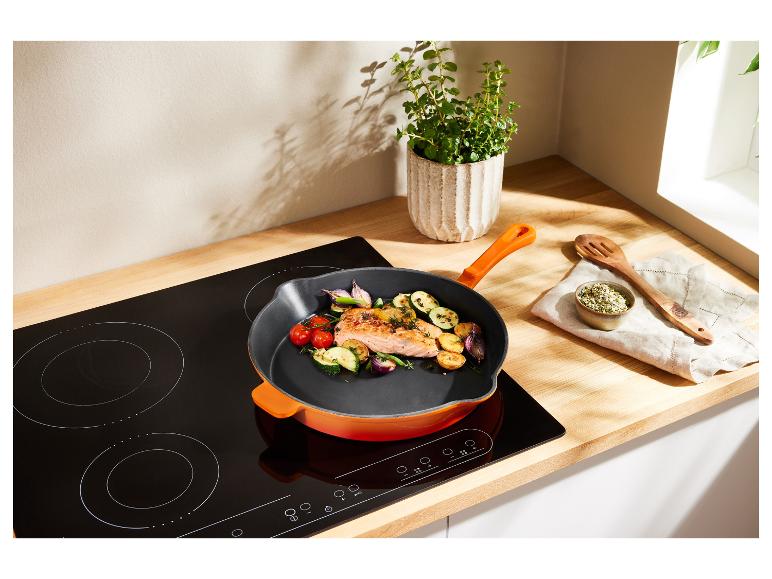 Eine orangefarbene Pfanne mit Lachs und Gemüse auf einem Induktionskochfeld.