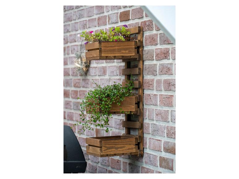 Vertikaler Wandgarten aus Holz mit Blumen und Grünpflanzen an einer Ziegelwand.