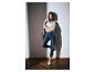 Frau in Jeans, Sport-BH und Jacke, lehnt an einer Wand.
