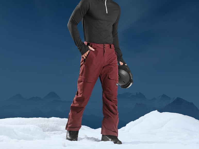 Mann in roten Skihosen und schwarzem Helm vor Bergen.