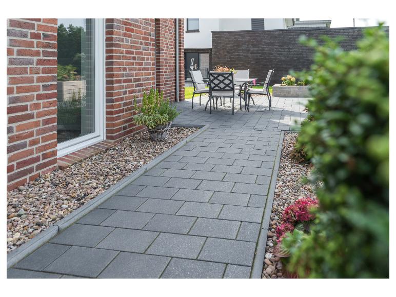 Moderne Terrasse mit grauen Pflastersteinen, Gartenmöbeln und Backsteinhaus.