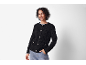 Lächelnde Frau in schwarzer strukturierter Strickjacke und Jeans, Hand in der Tasche.