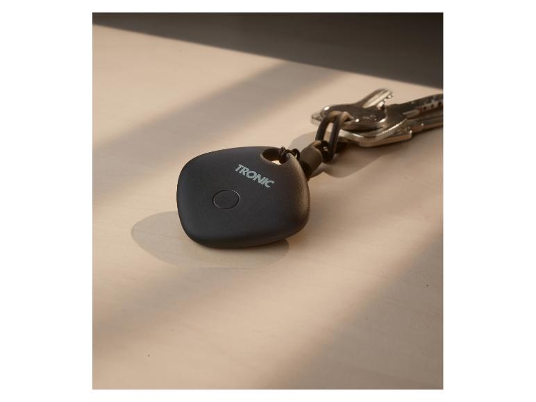 Schwarzer Schlüsselfinder mit „TRONIC“-Schriftzug und einem Schlüsselbund auf einem Holztisch.