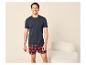Mann in marineblauem T-Shirt und rot karierten Boxershorts, lächelnd in einem hellen Raum.