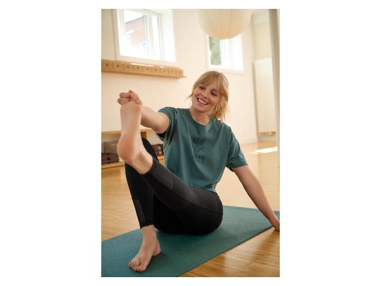Frau in grünem T-Shirt und schwarzen Leggings dehnt sich auf einer Yogamatte.