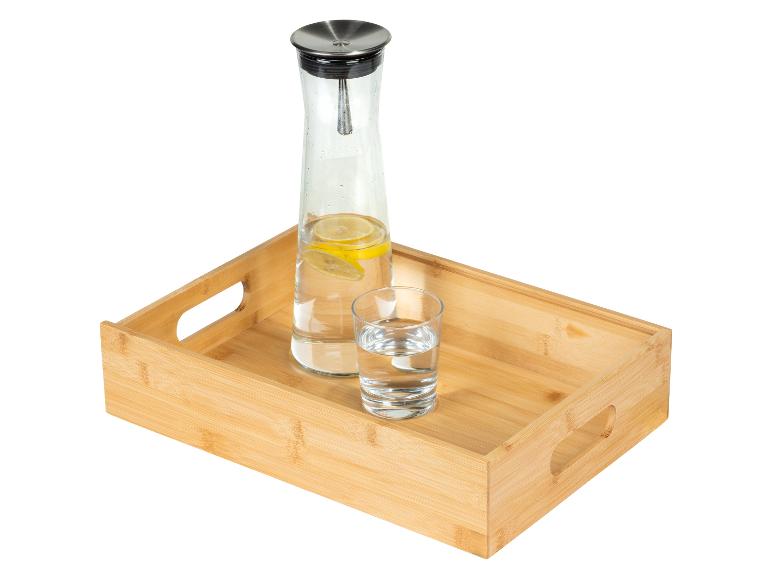 Karaffe mit Zitronenwasser und Glas auf einem Bambustablett.