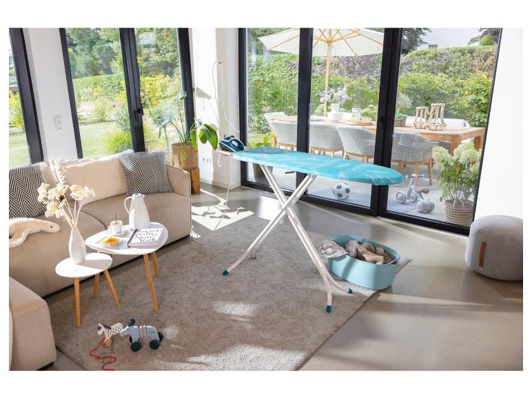 Bügelbrett mit Bügeleisen in einem hellen Wohnzimmer mit Gartenblick.
