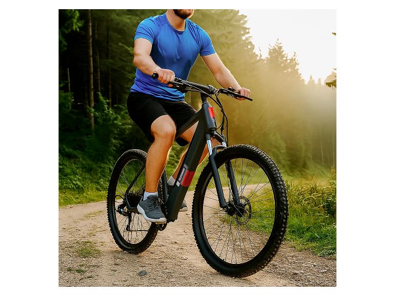 Mann fährt E-Mountainbike auf Waldweg bei Sonnenuntergang.