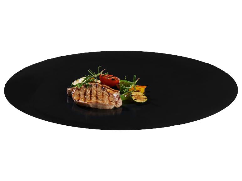 Gegrilltes Schweinekotelett mit gegrilltem Gemüse und Rosmarin auf einem schwarzen Teller.