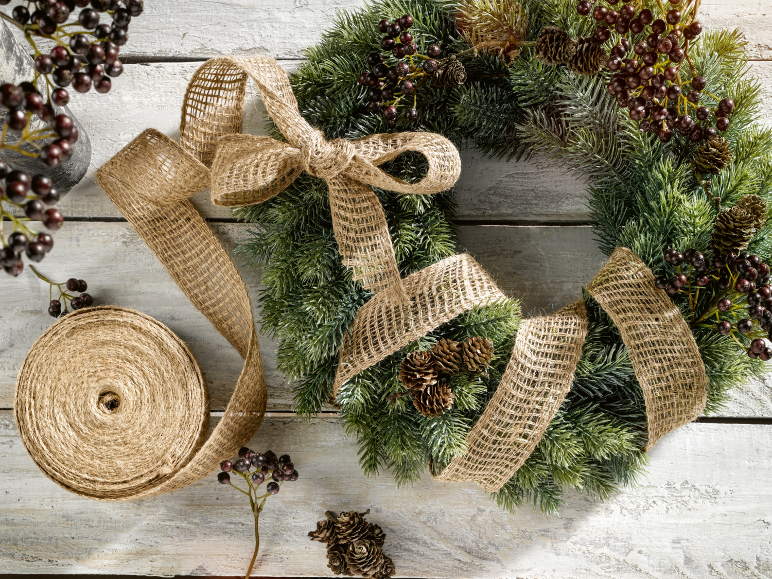 Weihnachtskranz mit Juteband und Beeren auf weißem Holzhintergrund.