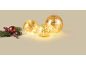 Drei leuchtende goldene LED-Glaskugeln neben einem dekorativen Kiefernzweig mit roten Beeren