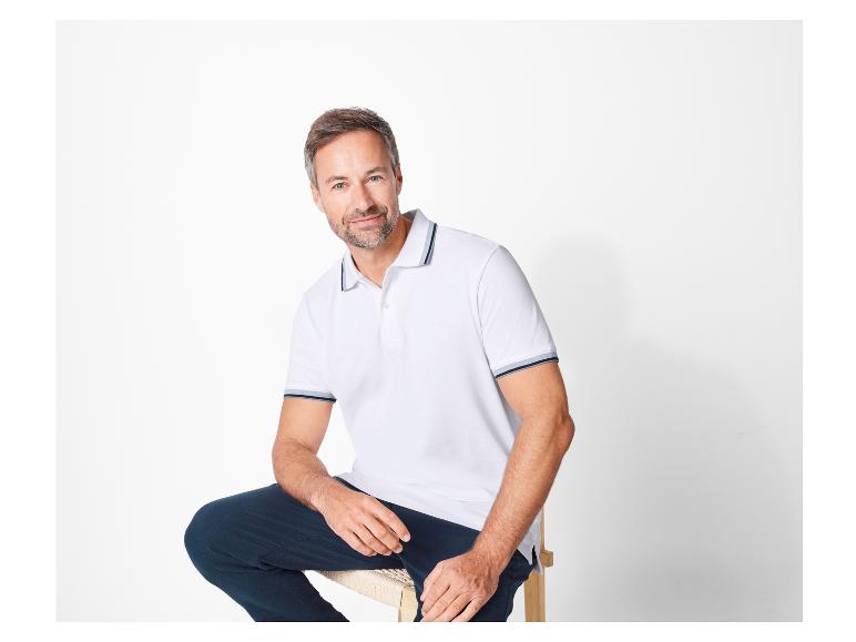 Mann in weißem Poloshirt und dunkler Hose.