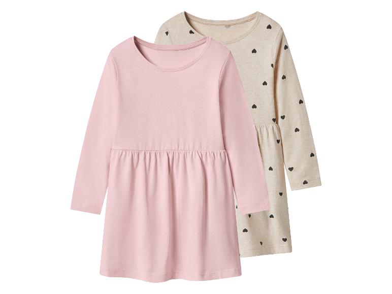 Zwei langärmlige Kinderkleider, eines unifarben rosa und eines beige mit schwarzen Herzen.