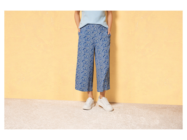 Eine Frau trägt weiße Sneaker und blaue, gemusterte Hosen.