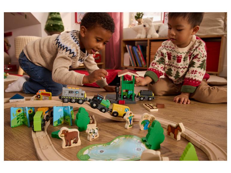 Zwei Kinder spielen mit einer Holzeisenbahn und einem Bauernhof-Spielset.