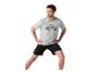 Mann in grauem T-Shirt mit schwarzem Aufdruck und schwarzen Shorts beim Dehnen
