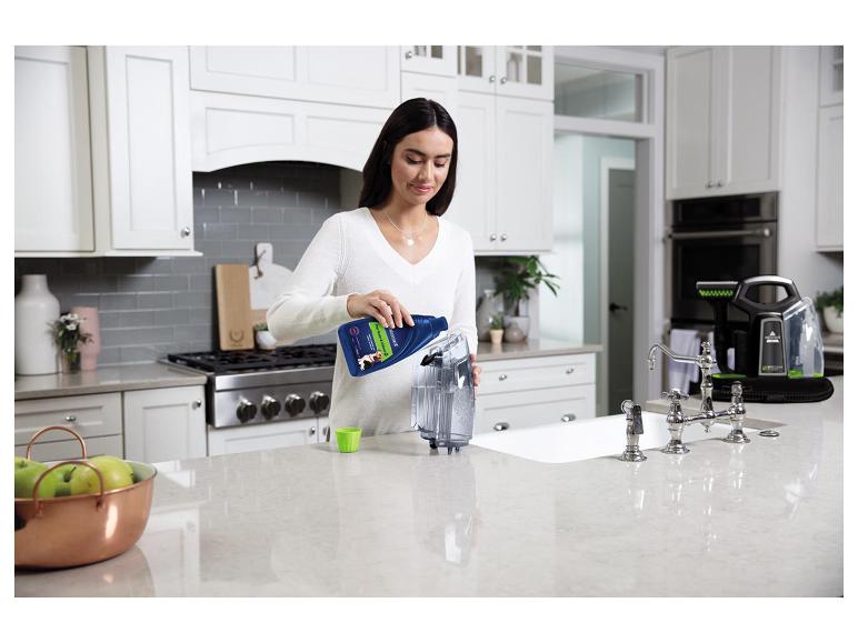 Frau gießt Tierfleckenentferner in einen tragbaren Reiniger in der Küche.