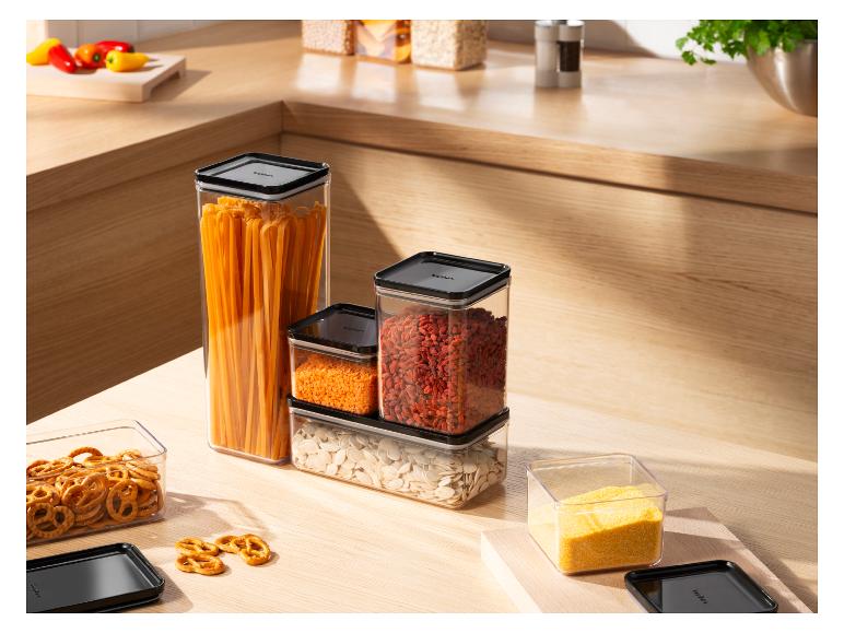 Transparente Vorratsbehälter mit schwarzen Deckeln, gefüllt mit Nudeln, Linsen, Goji und Samen.