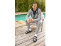 Mann in grauem Trainingsanzug und schwarzen Sandalen mit weißen Socken, lächelt und hält einen grünen Smoothie.