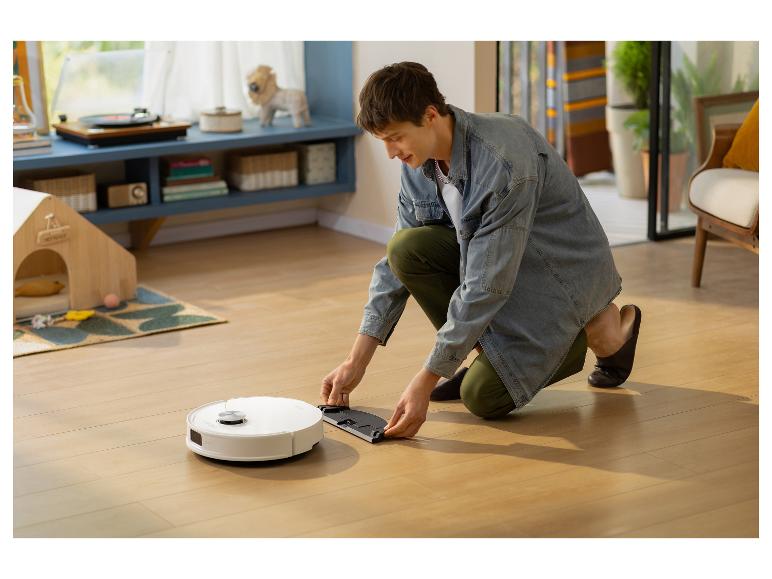 Mann befestigt Wischzubehör an einem Saugroboter auf einem Holzboden.