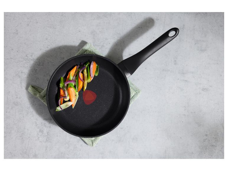 Schwarze Bratpfanne mit geschnittenem Gemüse (Karotten, Zwiebeln, Spargel) auf einem grünen Tuch.