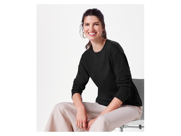 Eine Frau trägt ein schwarzes Langarmshirt und eine beige Hose.