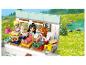 Drei Lego Friends Figuren genießen Sandwiches und Getränke in einem Wohnmobil, mit einer grünen Landschaft im Hintergrund.