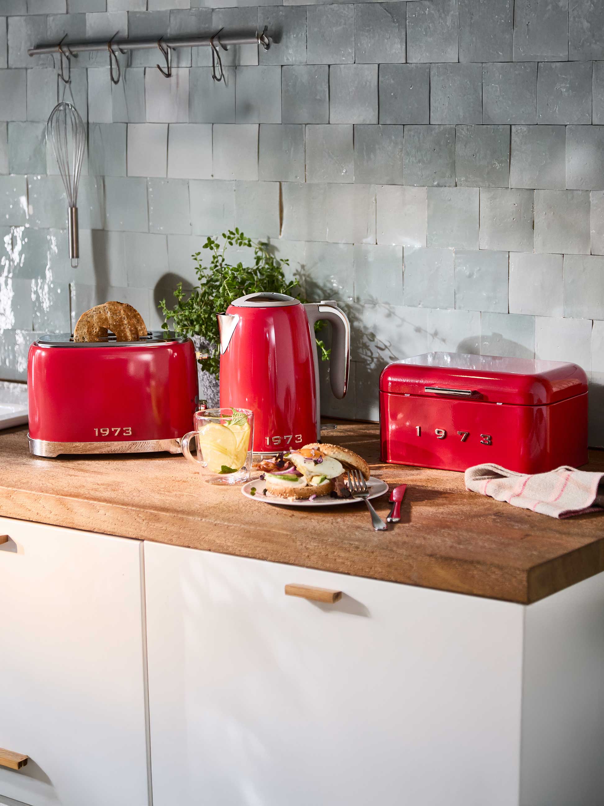 Roter Toaster, Wasserkocher und Brotkasten mit Frühstück auf einer Holztheke.