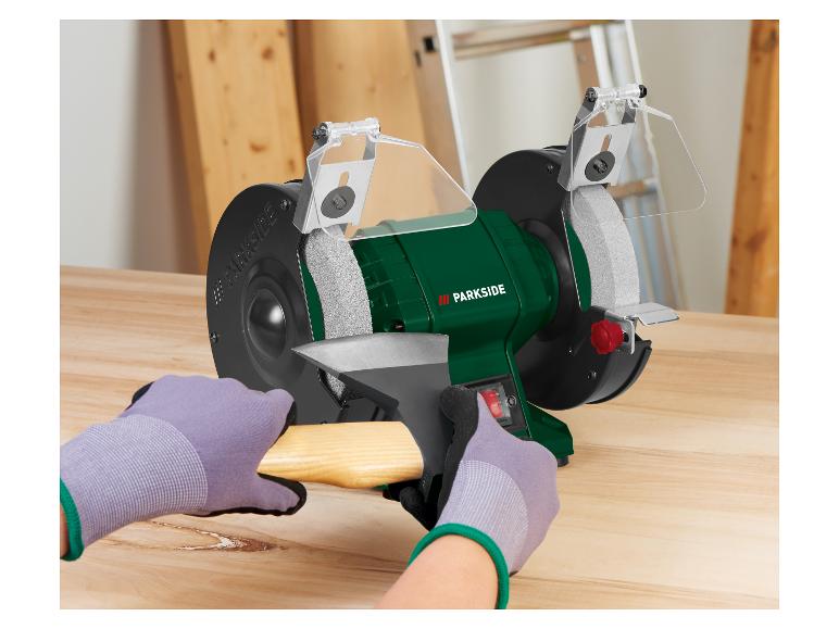 Parkside Schleifbock schärft eine Axt, mit behandschuhten Händen.
