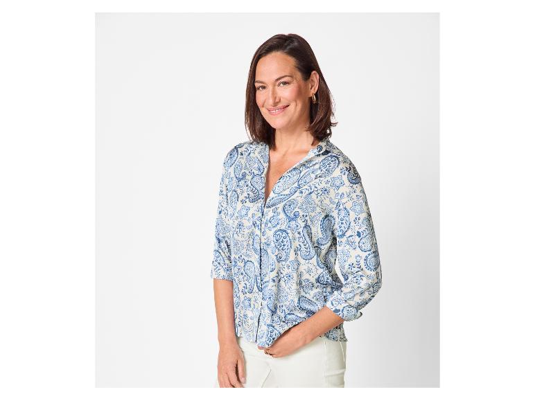 Lächelnde Frau in blau-weiß gemusterter Bluse und weißer Hose.