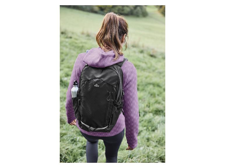 Eine Frau mit einem schwarzen Crivit-Rucksack geht über Gras.