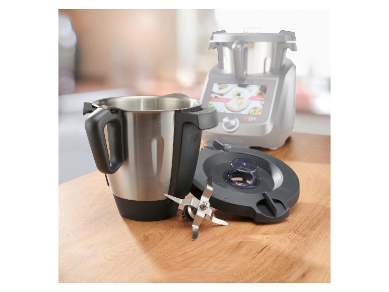 Edelstahl-Mixbehälter mit Klingen und Deckel, mit Küchenmaschine im Hintergrund.