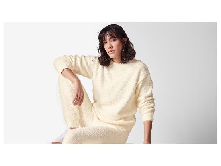 Frau in cremefarbenem Fleece-Pullover und Hose auf weißem Hintergrund.