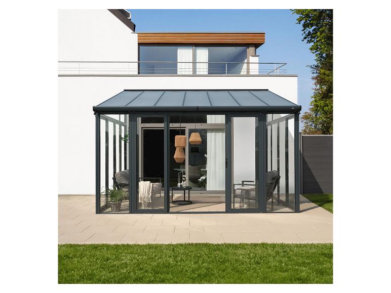 Ein Glas-Wintergarten mit dunkelgrauen Rahmen und Möbeln, vor einem Haus und Rasen.