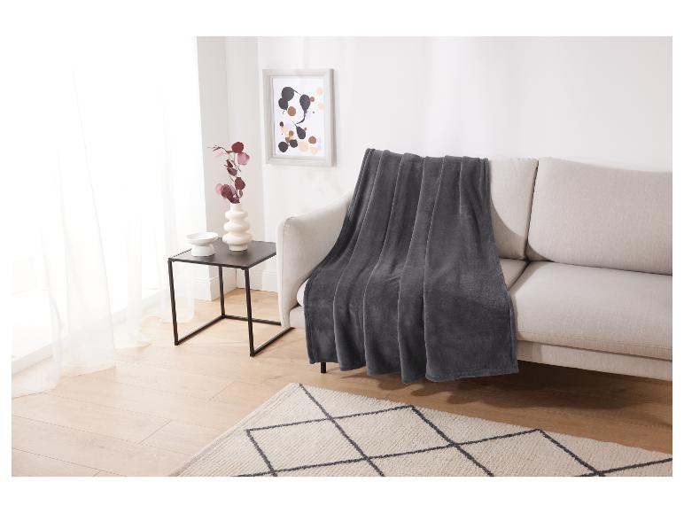 Eine graue Decke auf einem beigen Sofa in einem modernen Wohnzimmer.