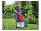 Mann zerkleinert Gartenabfälle mit einem roten Gartenhäcksler in einem grünen Garten.