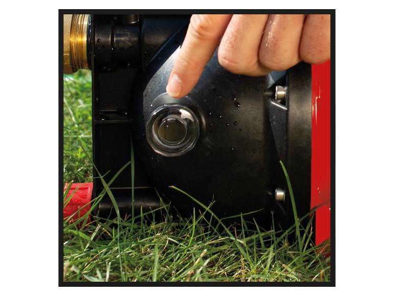 Eine Hand drückt einen transparenten Knopf an einer schwarz-roten Wasserpumpe im Gras.