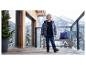 Kleiner Junge in Winterjacke und Jeans auf verschneitem Balkon mit Berglandschaft.