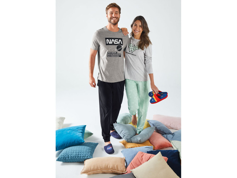 Mann und Frau in Pyjamas mit NASA und Wonder Woman-Prints, stehend auf Kissen.