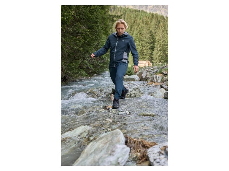 Mann in Wanderjacke und Hose überquert einen Fluss.