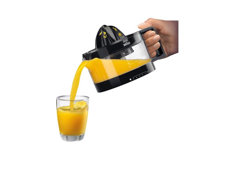 Hand gießt frisch gepressten Orangensaft aus einer Zitruspresse in ein Glas.