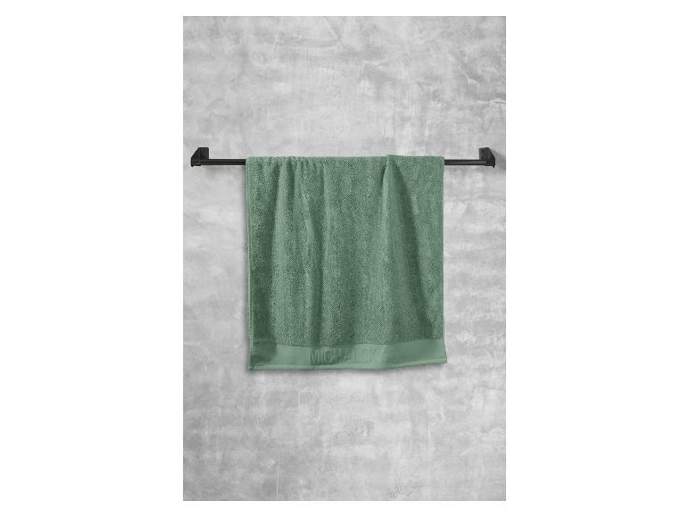 Ein grünes Handtuch von Michael Kors hängt an einem schwarzen Handtuchhalter.