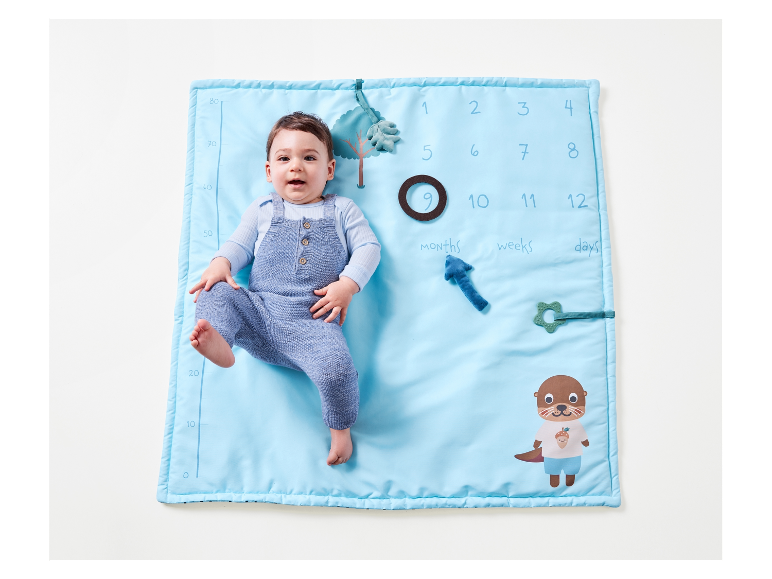 Ein Baby liegt auf einer blauen Spielmatte mit Zahlen und Tieren.