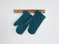 Zwei blaue Ofenhandschuhe hängen an einem Holzgestell.