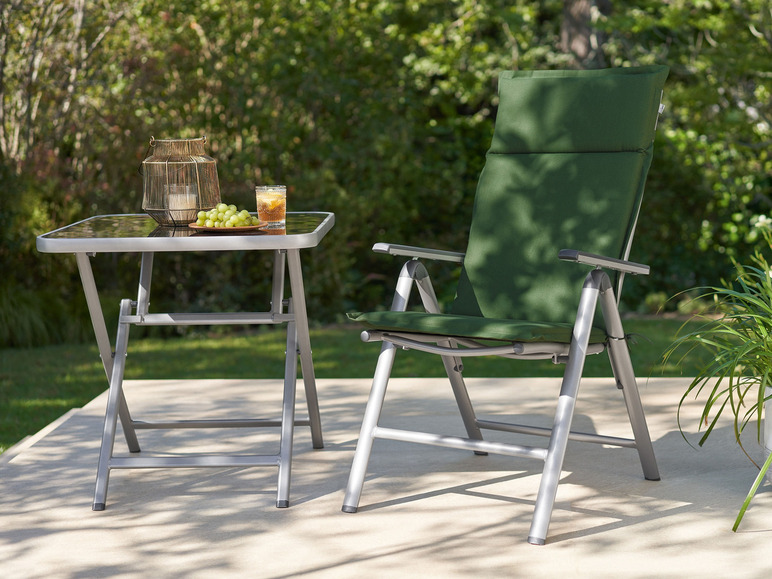Ein grüner Klappstuhl und ein Tisch mit Glasplatte im Garten.