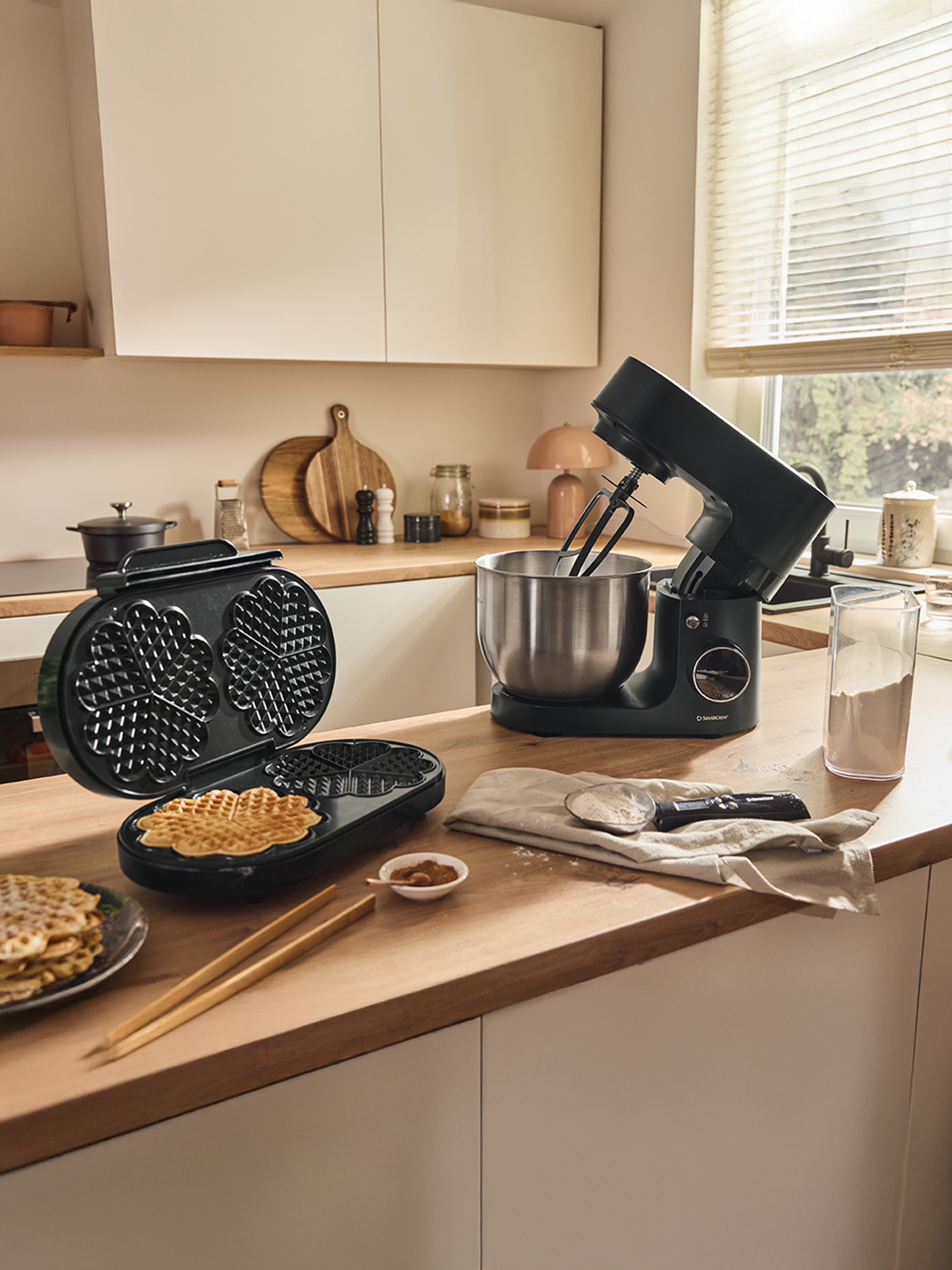 Ein Waffeleisen und ein schwarzer Küchenmixer auf einer Holztheke, mit fertigen Waffeln.