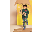 Lächelndes Kind in Regenjacke und Regenhose mit Superheldenmuster, hält einen Kartonschirm.