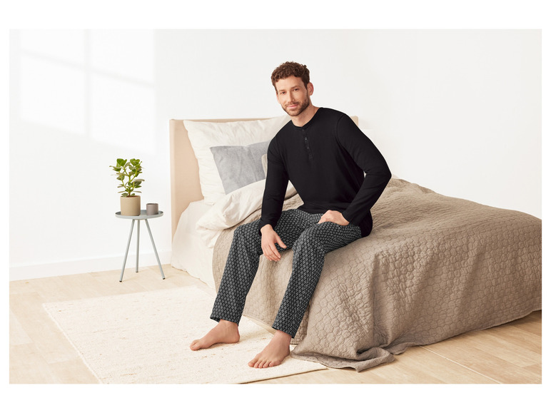 Mann in schwarzem Pyjama mit weißem Muster, sitzt auf einem Bett