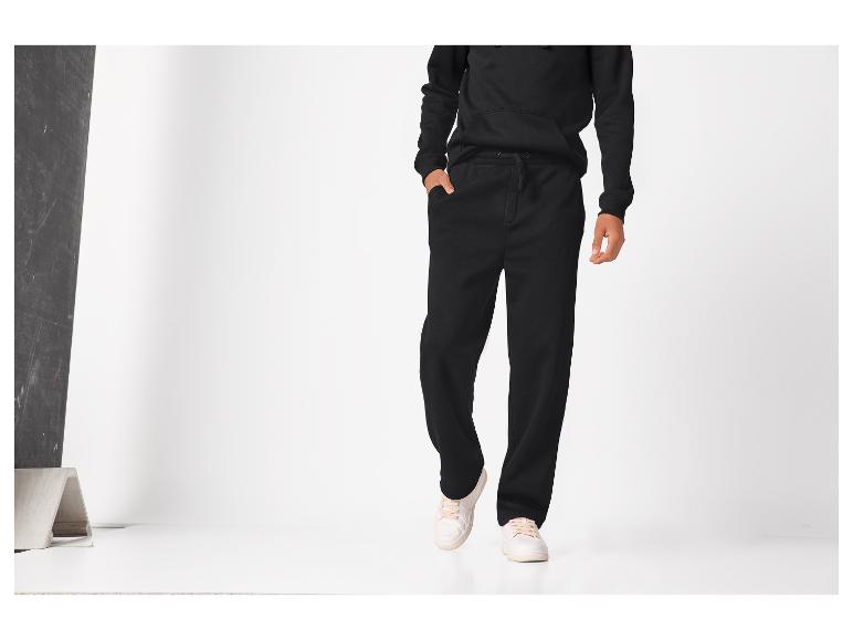 Person in schwarzem Hoodie und schwarzer Jogginghose mit hellen Sneakern